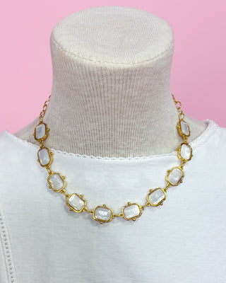Gold necklace with large beads on a mannequin against a pink background