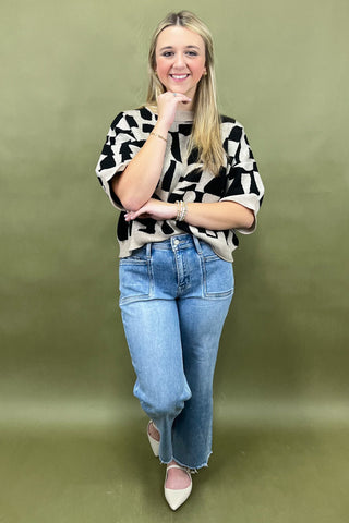 Woman wearing a black and white patterned sweater and blue jeans on a green background