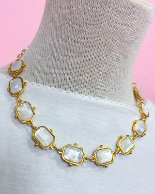 Necklace with gold accents and white stones on a mannequin against a pink background