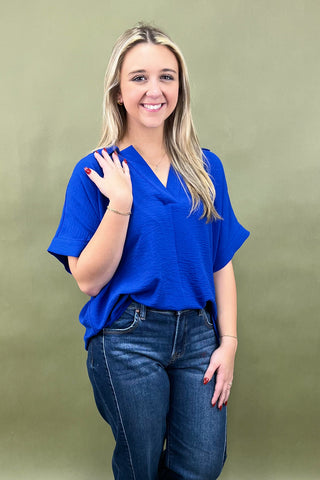 Woman wearing a blue top and jeans against a green background