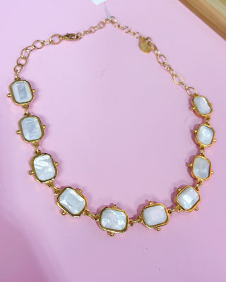 Necklace with gold and white stone design on a pink background