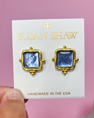 Gold-framed blue earrings on a Susan Shaw branded card with a pink background