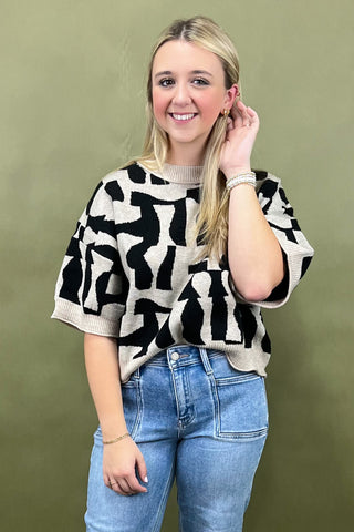 Woman wearing a black and white patterned sweater and blue jeans against a green background