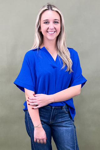 Woman wearing a blue top and jeans against a plain background