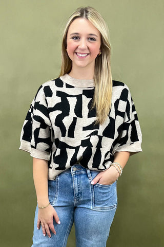 Woman wearing a black and white patterned sweater with blue jeans against a green background