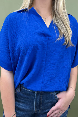 Person wearing a blue top and jeans against a green background