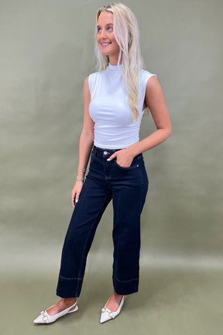 Woman wearing a white top and dark blue jeans against a plain background