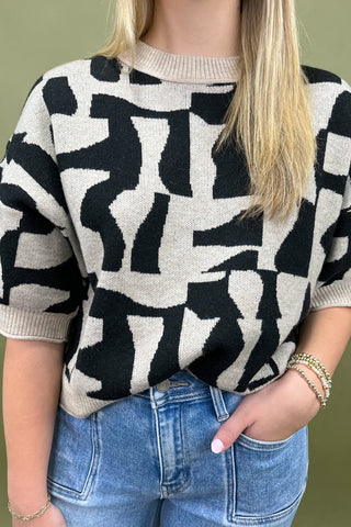 Person wearing a black and white patterned sweater with blue jeans against a green background