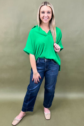 Woman wearing a green top and blue jeans against a beige background