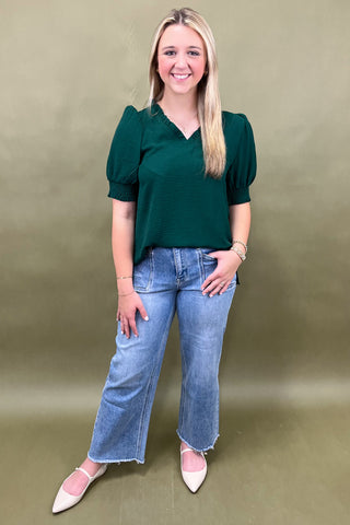 Woman wearing a green blouse and blue jeans against a beige background