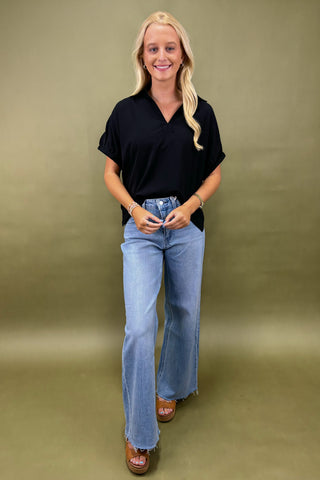 Woman wearing a black top and blue jeans against a green background