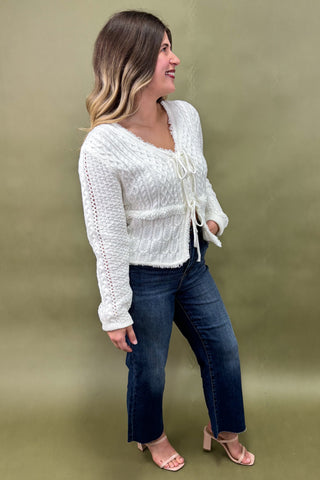 Woman wearing a white knit cardigan and blue jeans on a green background