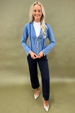 Woman wearing a blue denim jacket and dark jeans on a green background