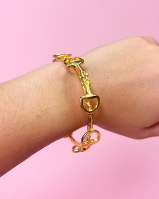 Gold bracelet with unique design on a wrist against a pink background