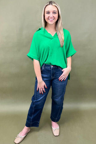 Woman wearing a green top and blue jeans against a plain background