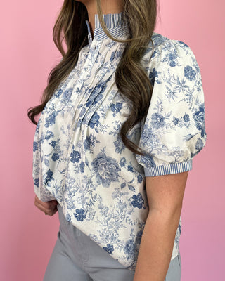 Woman wearing a blue floral blouse with puffed sleeves against a pink background