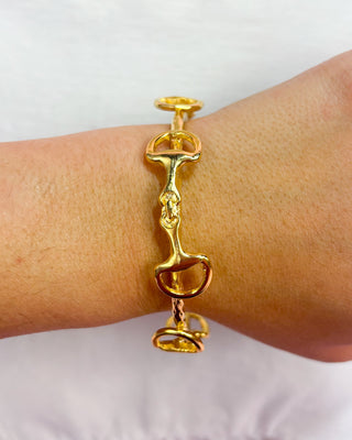 Gold bracelet with horse and rider design on a wrist against a white background
