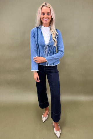 Woman wearing a blue denim jacket and dark jeans on a green background