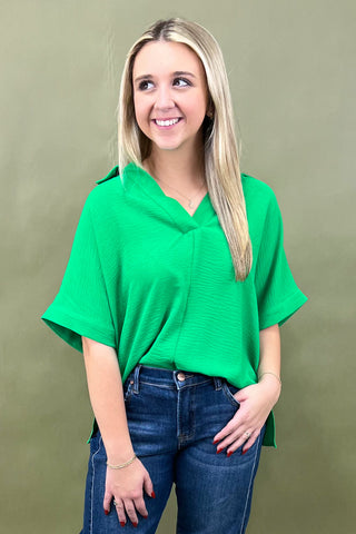 Woman wearing a green top and blue jeans against a beige background