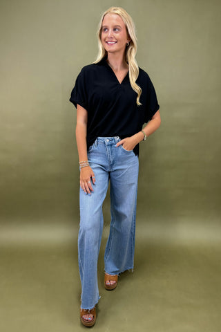 Woman wearing a black top and blue jeans against a green background