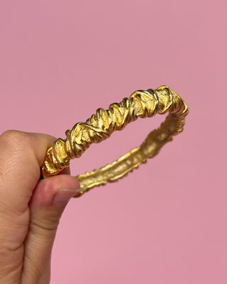 Gold headband held by a hand against a pink background