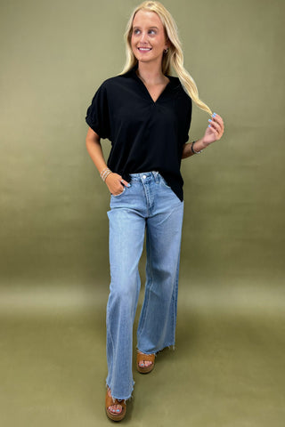 Woman wearing a black top and blue jeans against a green background