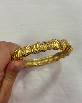 Gold bracelet held by a hand against a light background