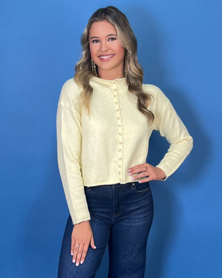 Soft butter yellow button-front knit cardigan with long sleeves, round neckline, and a relaxed cropped fit.