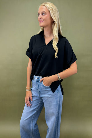 Woman wearing a black top and blue jeans against a green background