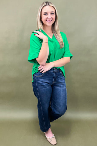 Woman wearing a green shirt and blue jeans against a beige background