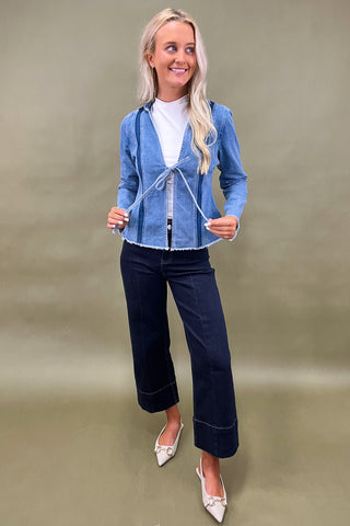 Woman wearing a blue denim jacket and dark jeans on a green background