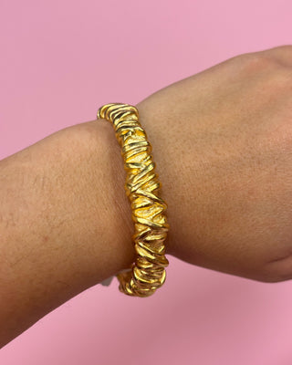 Gold bracelet on a wrist with a pink background