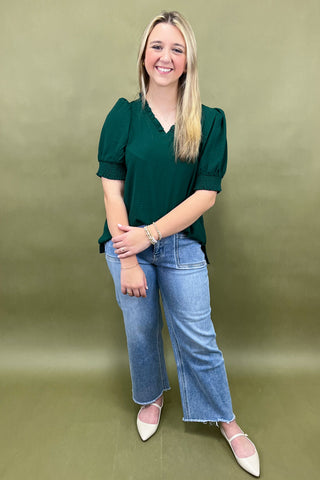 Woman wearing a green top and blue jeans against a green background