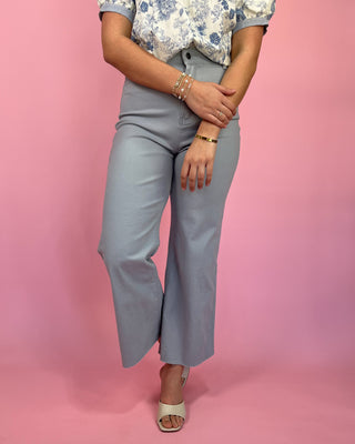 Person wearing a floral top and gray wide-leg pants on a pink background