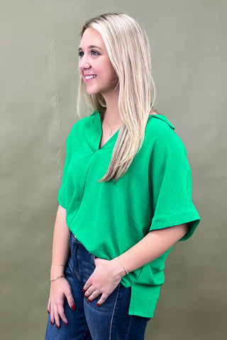 Woman wearing a green top and blue jeans against a plain background