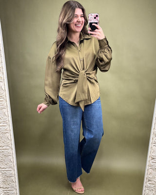 Woman taking a mirror selfie wearing a green top and blue jeans on a green background