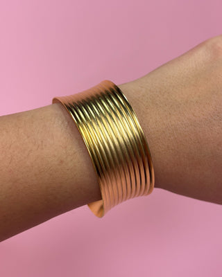 Gold bangle on a wrist with a pink background