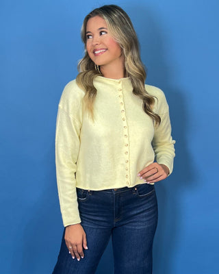 Soft butter yellow button-front knit cardigan with long sleeves, round neckline, and a relaxed cropped fit.