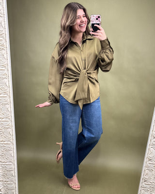 Woman taking a mirror selfie wearing a green blouse and blue jeans on a green background