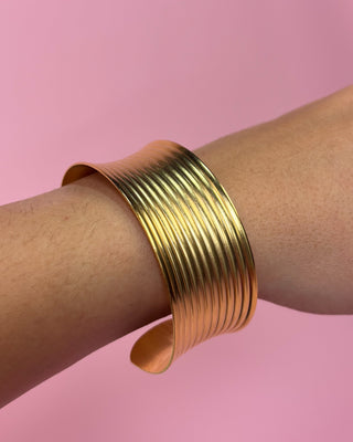 Gold bracelet on a wrist with a pink background