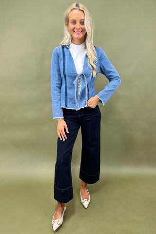 Woman wearing a blue denim jacket and dark jeans on a green background