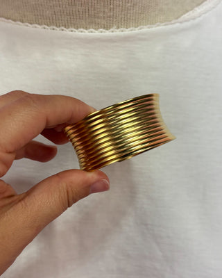 Gold bracelet held by a hand against a white background