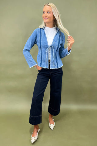 Woman wearing a blue denim jacket and dark jeans on a green background