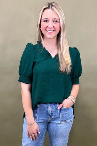 Woman wearing a green blouse and blue jeans against a beige background