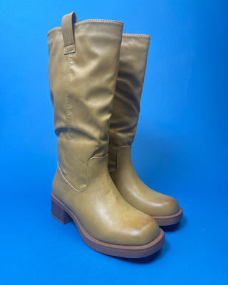 A tan leather knee-high boot with a brown stacked heel, held up against a solid blue background.