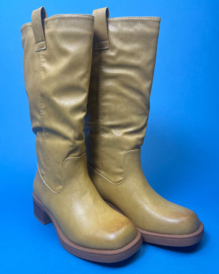 A tan leather knee-high boot with a brown stacked heel, held up against a solid blue background.
