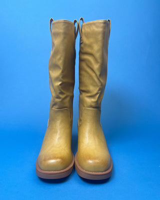 A tan leather knee-high boot with a brown stacked heel, held up against a solid blue background.