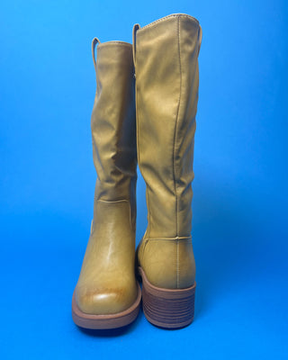 A tan leather knee-high boot with a brown stacked heel, held up against a solid blue background.