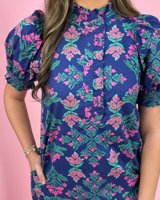 Woman wearing a blue floral dress with pink and green flowers on a pink background