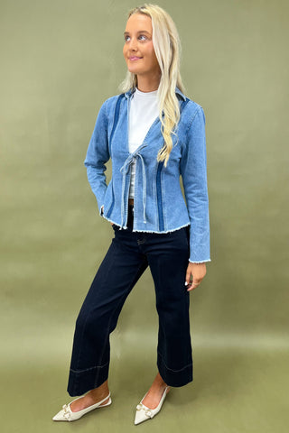 Woman wearing a blue denim jacket and dark jeans on a green background